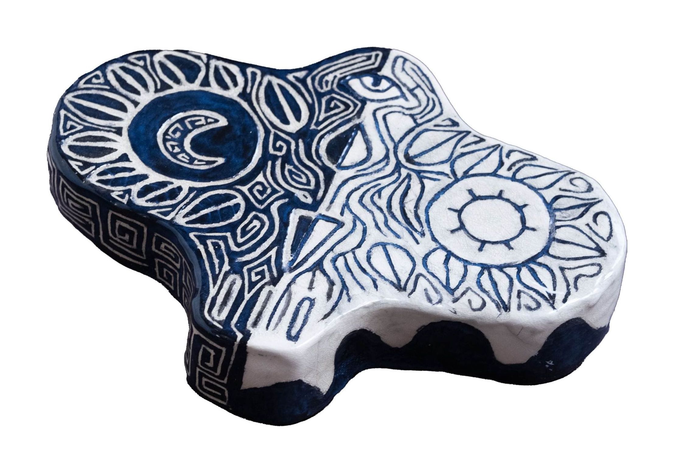 Flat ceramic piece with an irregular outline, glazed deep blue and white, carved with a sun on one side, a crescent moon on the other and swirling patterns between.