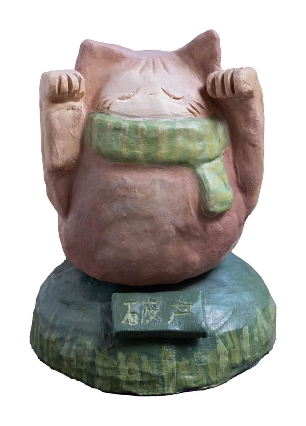 Ceramic sculpture of a pink cat with closed eyes and both paws raised, wearing a green scarf, sitting on a green base with a small sign reading 破产 (bankruptcy).